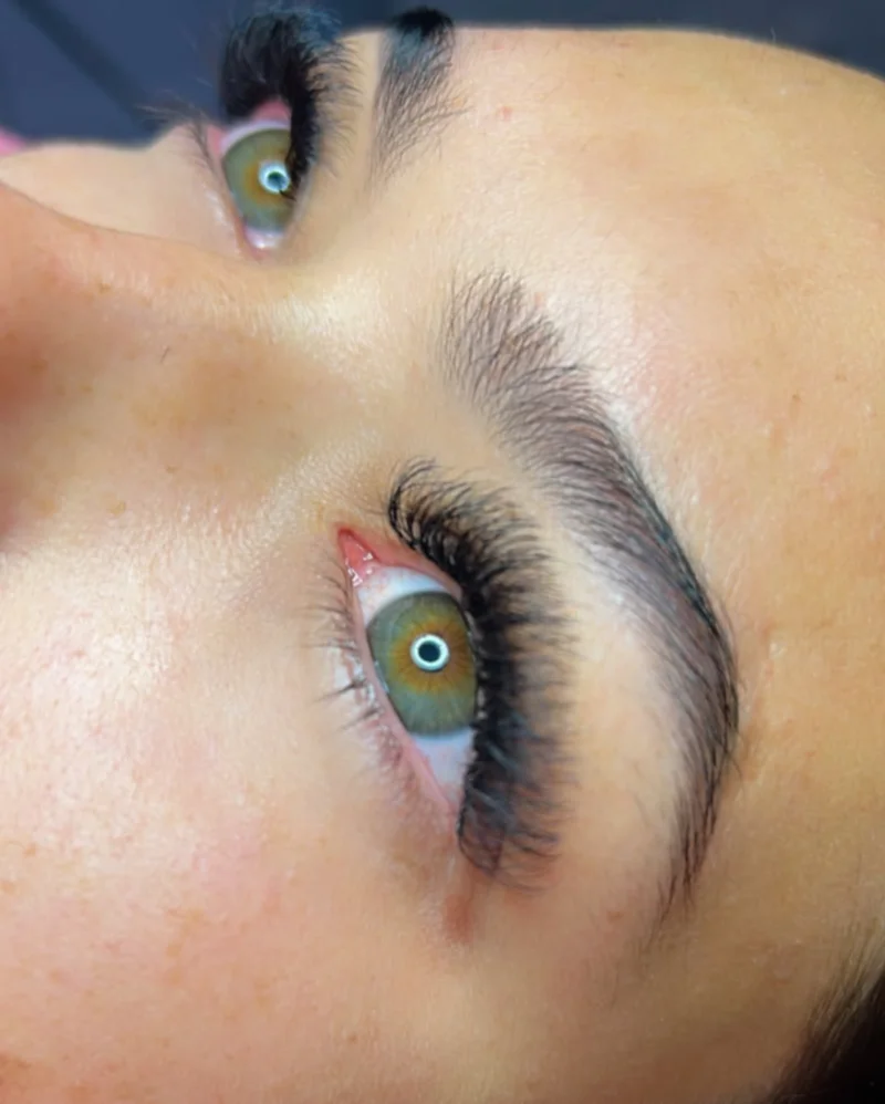Close dos olhos de uma cliente com extensão de cílios e sobrancelhas feitas na Estética Ela Bela